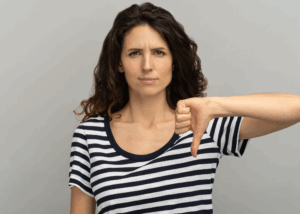 Brunette female with long hair wearing a black and white horizontal striped crew neck shirt with a disappointed look and gesturing thumb down.