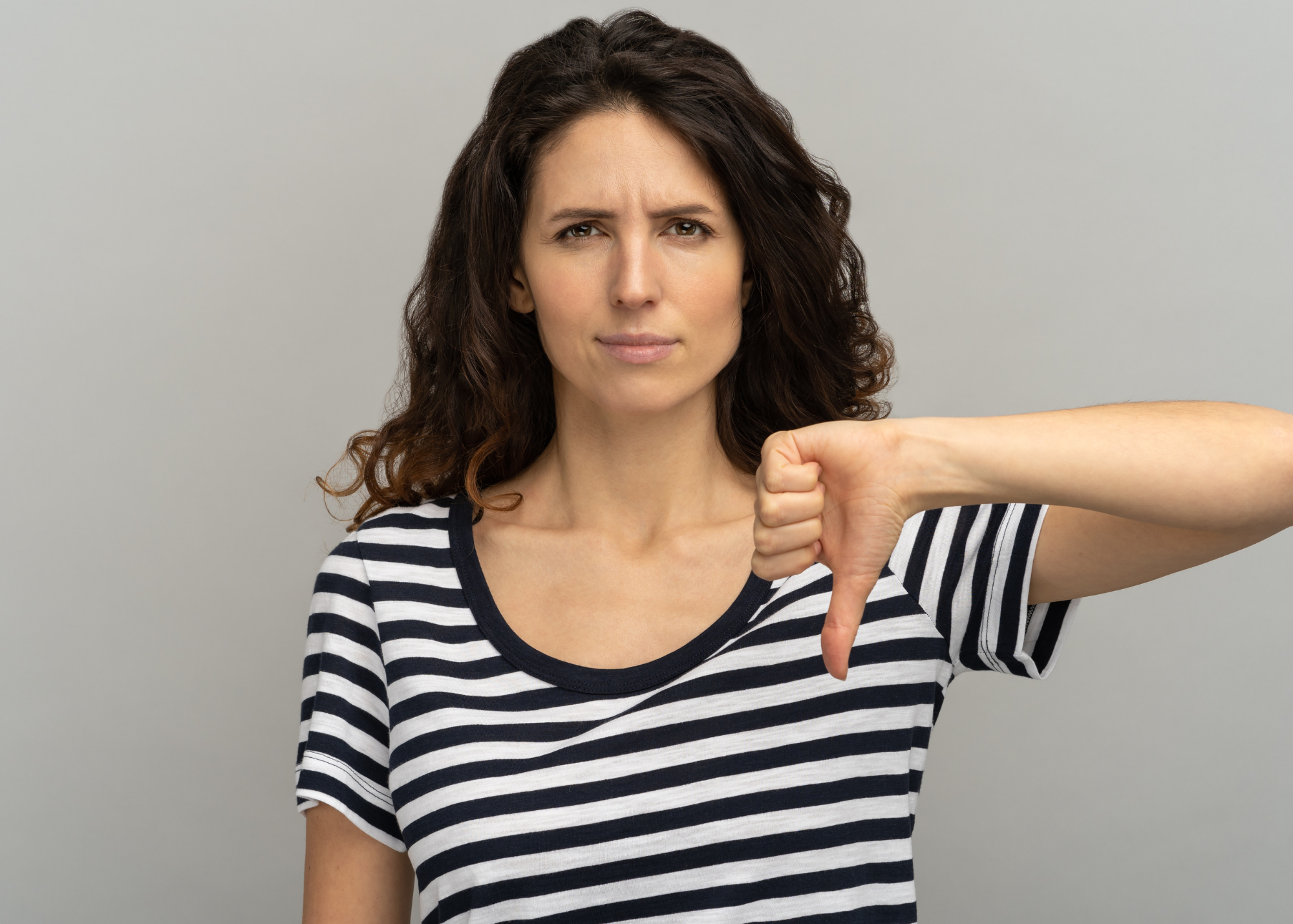 Brunette female with long hair wearing a black and white horizontal striped crew neck shirt with a disappointed look and gesturing thumb down.